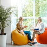 Two individuals speaking with one another sitting on beanbag chairs.
