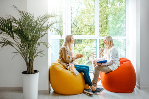 Two individuals speaking with one another sitting on beanbag chairs.